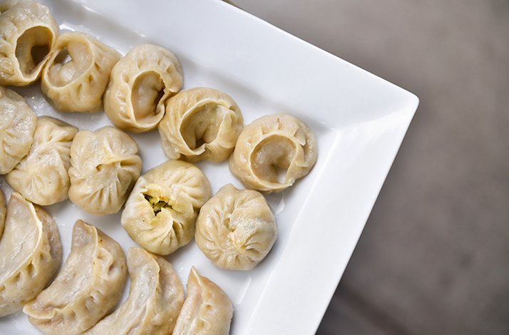 Assorted steamed dumplings arranged on a white rectangular serving platter, with pleated tops and filled wrappers visible.