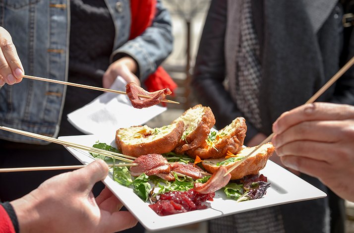 Three people sharing a white plate of stuffed bread, cured meat, and mixed greens during private guided Kensington Market food tour.
