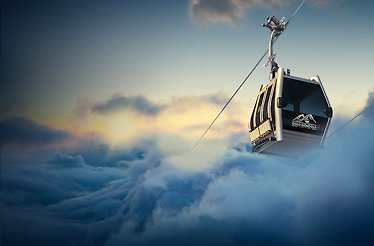 A group of passengers inside a cable car glide through the sky in clouds.