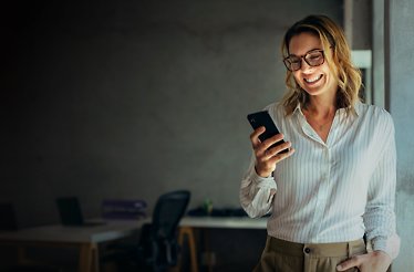 A lady in a business attire using a smartphone in a modern, minimalistic office setting