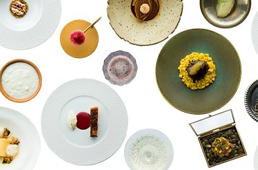 A top-down view of assorted plated dishes and beverages, including grains, meats, desserts, and garnishes, arranged on a white background.