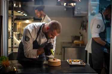 A chef preparing a dish using molecular gastronomy techniques in the kitchen of Delirium Silence.