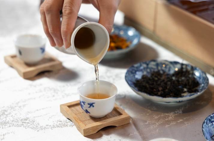 Tea is being poured into a small porcelain cup on a bamboo tray.
