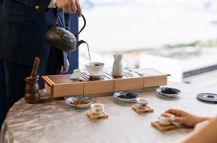 Hot water is being poured into a gaiwan on a wooden tea tray.