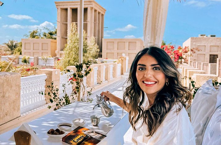 Woman pouring traditional tea on a rooftop cafe overlooking historic wind towers in Al Fahidi, Dubai.