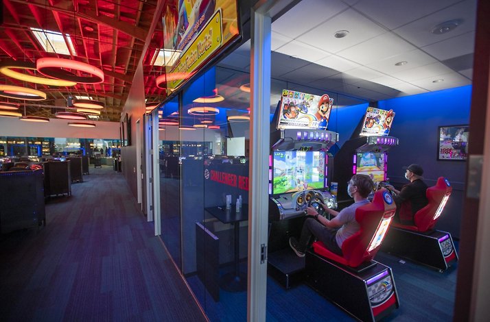 People playing Mario Kart arcade machines in a dedicated gaming room.