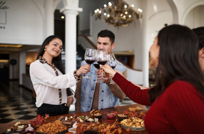 A group of friends are gathered around a table, raising their glasses of red wine in a toast, inside Casa Viñamar.