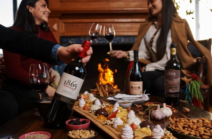 A group of people are enjoying San Pedro 1865 wine served with platter of cheese, nearby a fireplace at Casa Viñamar.