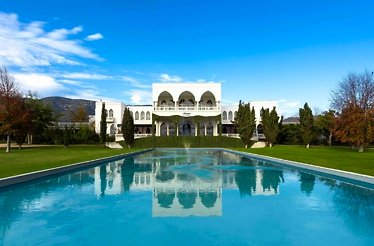 A shot of Casa Viñamar, showcasing it's white, multi-story building with arched windows, situated in front of a pool.
