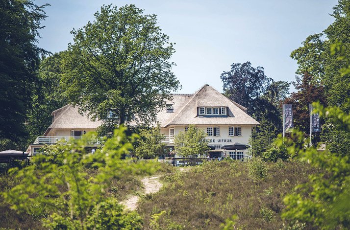 A wide shot of Landgoed de Uitkijk hotel, situated behind bushes of trees