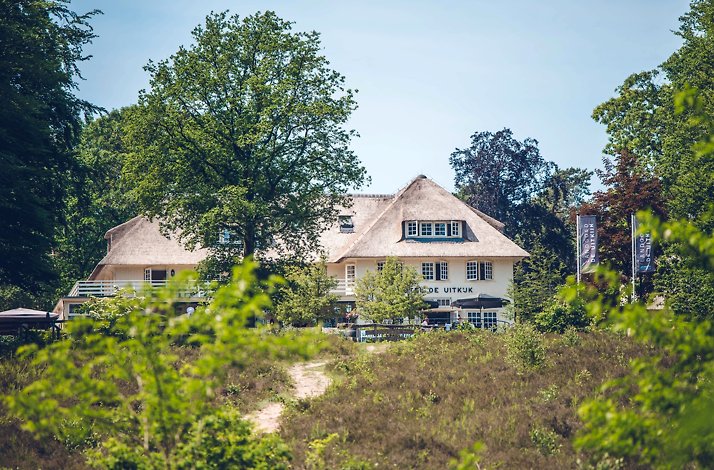 A wide shot of Landgoed de Uitkijk hotel, situated behind bushes of trees.