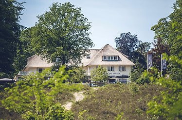 A wide shot of Landgoed de Uitkijk hotel, situated behind bushes of trees