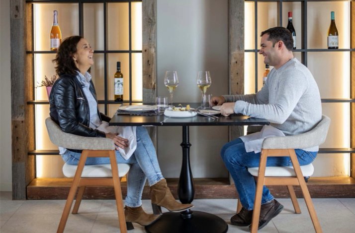 A couple sitting at a minimalist table in a stylish dining area with wine shelves in the background at Luxury Enoresort