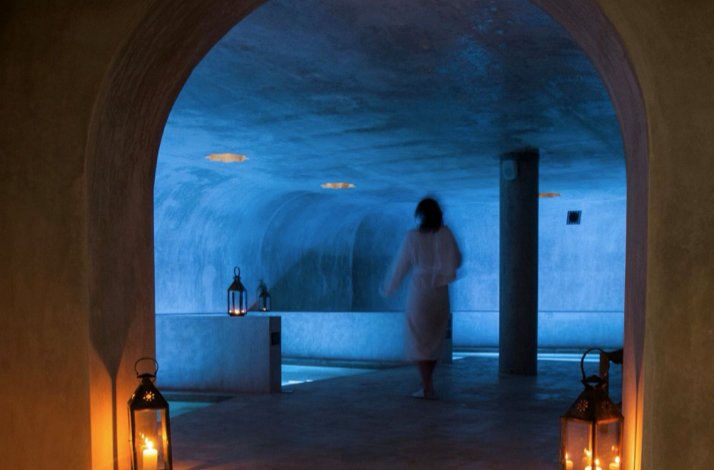 A person walks into a dimly lit indoor spa pool area illuminated by lanterns.