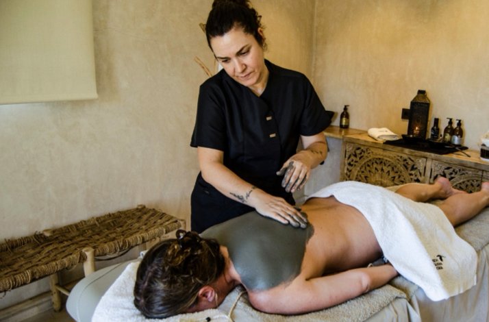 A spa therapist applies a mud treatment to a guest's back in a serene massage room.