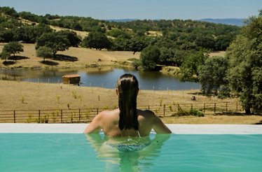 Guest relaxing in an infinity pool overlooking a lake and forested hills at Habitat Cigueña Negra.