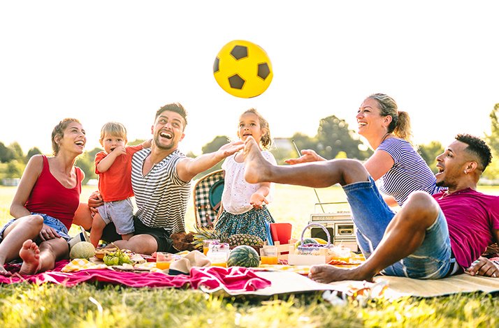A group of people enjoying a picnic on a blanket, with a bright yellow ball placed nearby.
