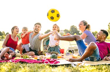 A group of people enjoying a picnic on a blanket, with a bright yellow ball placed nearby.
