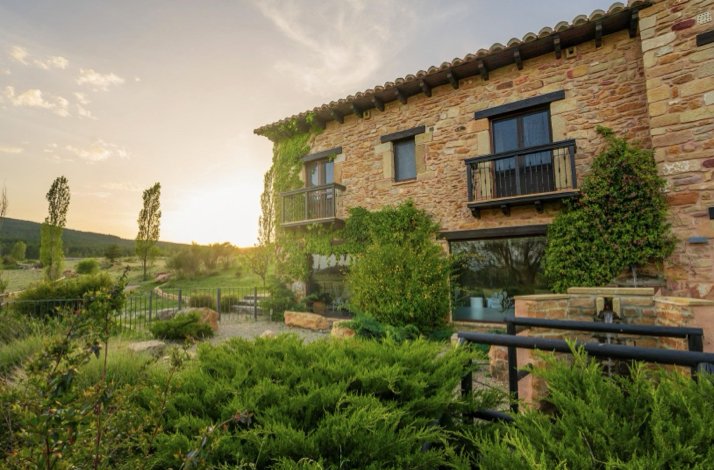 A stone hotel in the Sierra de Gúdar region with balconies, greenery, and a garden at sunset.
