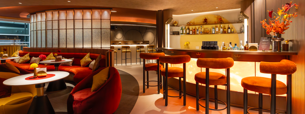 Wide view of Mastercard's exclusive airport dining club at Hong Kong International Airport, showcasing a curved bar, red velvet lounge seating, and warm lighting.