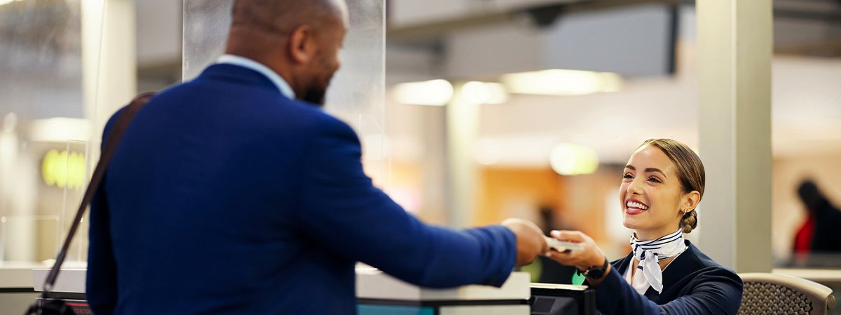 An Airport Assistant smiling and handing tickets to a person.