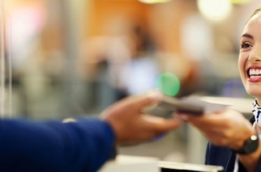 Smiling airport agent receiving travel documents from a suited traveller at a Fast Track security checkpoint