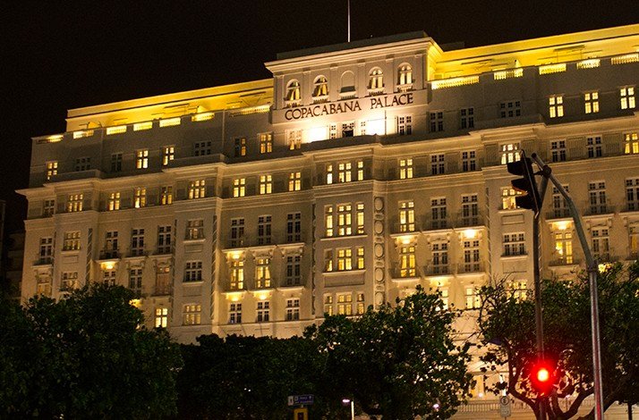 The illuminated facade of the historic Copacabana Palace hotel at night.