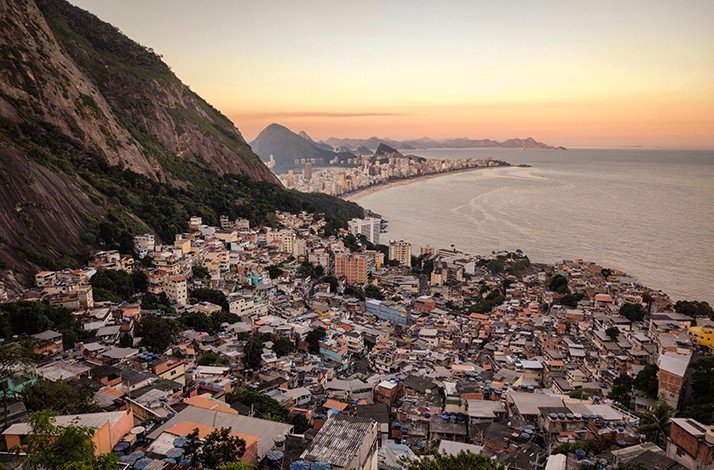 A sprawling favela nestled beside Morro Dois Irmãos contrasts with Rio's coastline at sunset.