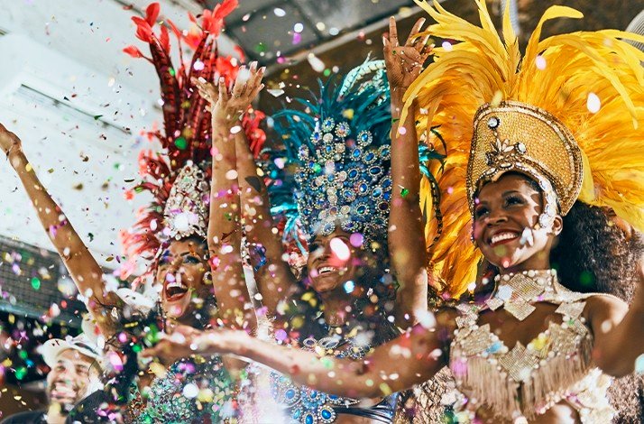 A group of people in vibrant Carnival costumes are celebrating, surrounded by colorful confetti.
