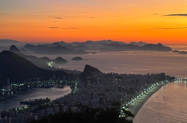 A breathtaking orange-hued sunset view of Rio with illuminated streets and distant mountains from Morro Dois Irmãos.
