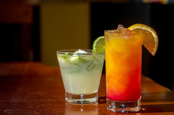 Two colorful cocktails on a wooden table, garnished with lime and orange slices served during the tour of Rio bars.