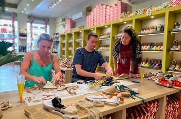 Three people engaged in shoe crafting at a store, with various shoes and materials visible around them.