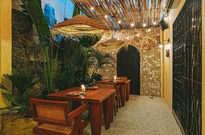 Intimate outdoor dining with wooden tables, lush greenery, and stone walls