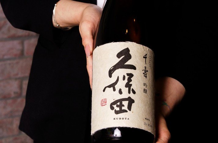 A waiter showing a bottle of sake served at ODDS & Zushi ANA