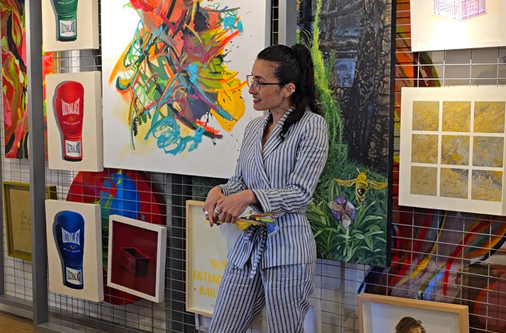 A person in striped attire stands in front of a vibrant wall of contemporary paintings at Culto Gallery.