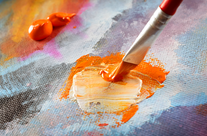 Close-up of a brush blending vibrant orange and white paint on a textured canvas
