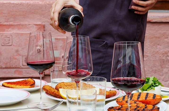Red wine being poured into glasses at a Buenos Aires table with milanesa and grilled sweet potatoes.