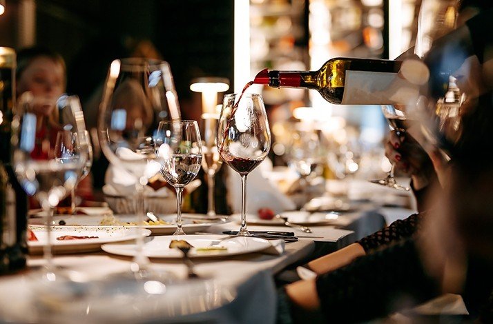 Wine being poured into a glass at a fine dining table setting.