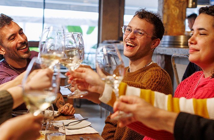 Glasses of white wine raised in a toast around a dining table.