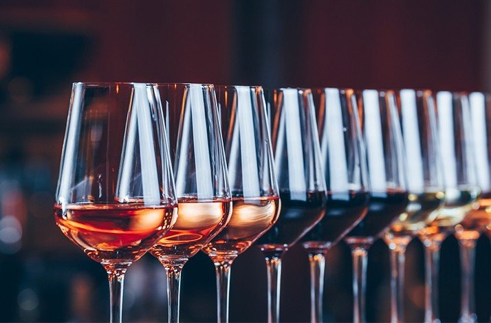 A row of wine glasses filled with wines of varying colors.
