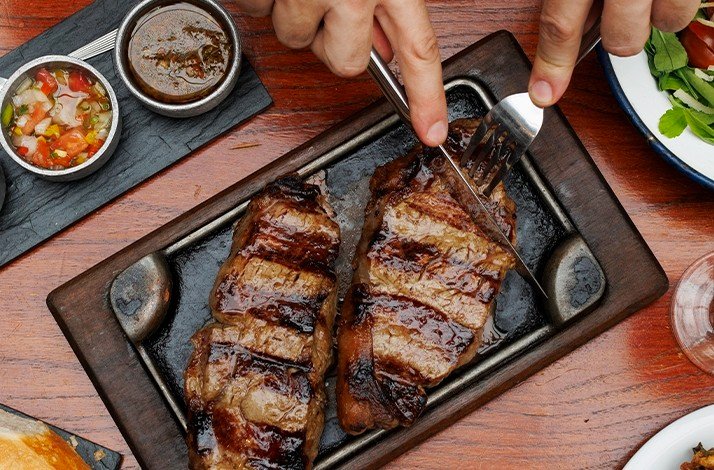 Grilled steak on a wooden platter with chimichurri and salsa on the side.