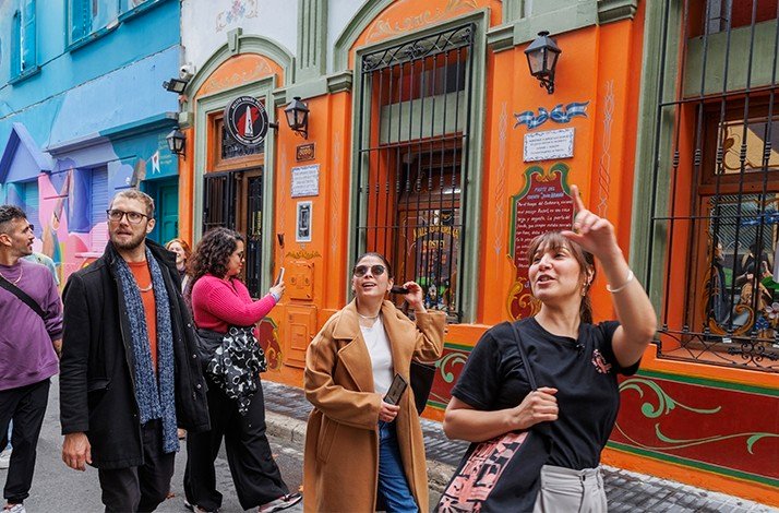 Group walking past colorful buildings in Buenos Aires, featuring ornate orange and green façades.