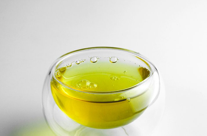 Glass cup filled with bright yellow-green olive oil.