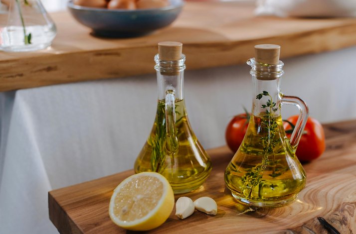 Glass bottles with infused olive oil and fresh herbs next to garlic, lemon, and tomatoes