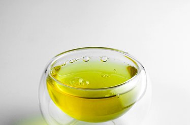 Glass cup filled with bright yellow-green olive oil.