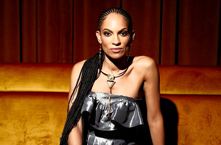 Promotional banner for Goapele in a silver ruffled top and gold necklace sits on a velvet couch.