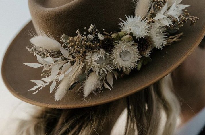 A brown hat featuring a rustic floral arrangement with white and earthy tones