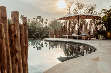 Scenic poolside with lounge chairs, umbrella, and tropical greenery at sunset