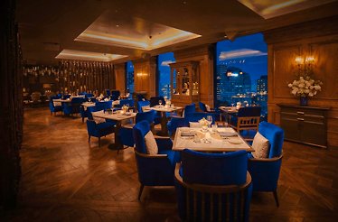 Albion Saigon restaurant's interior with tables featuring dark wooden flooring and royal blue chairs with panoramic city view.