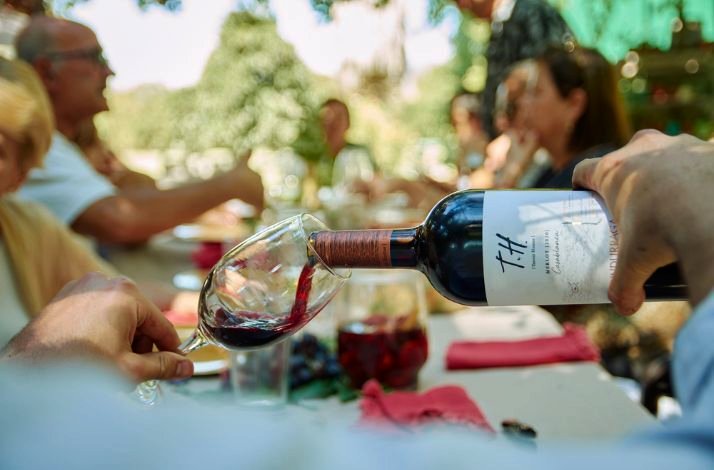 A bottle of red wine is being poured into a glass at an outdoor table setting